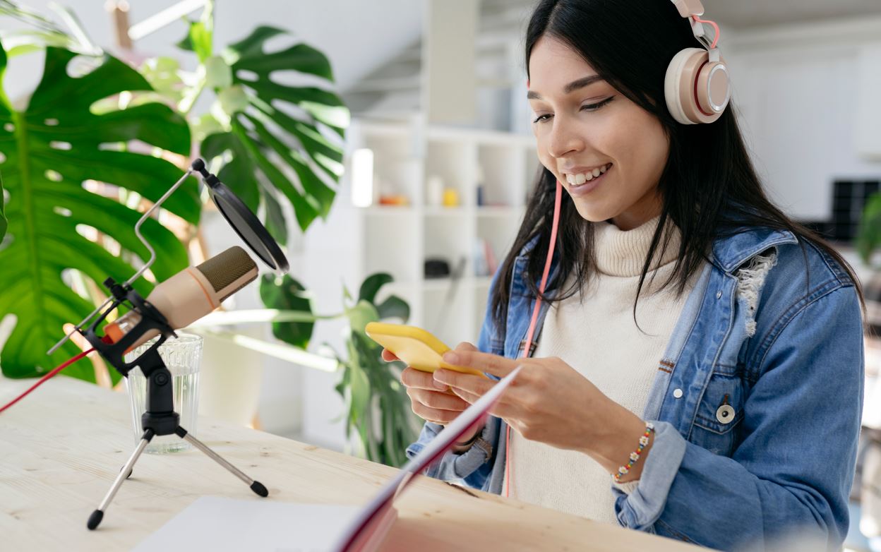 mulher fazendo um podcast com microfone notebook smartphone em casa