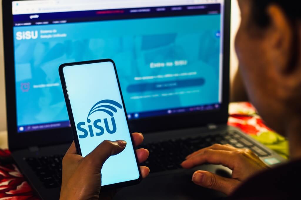 mulher vendo celular com app do Sisu e no computador à frente