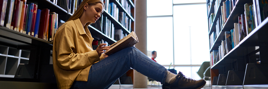 jovem lendo livro em biblioteca.