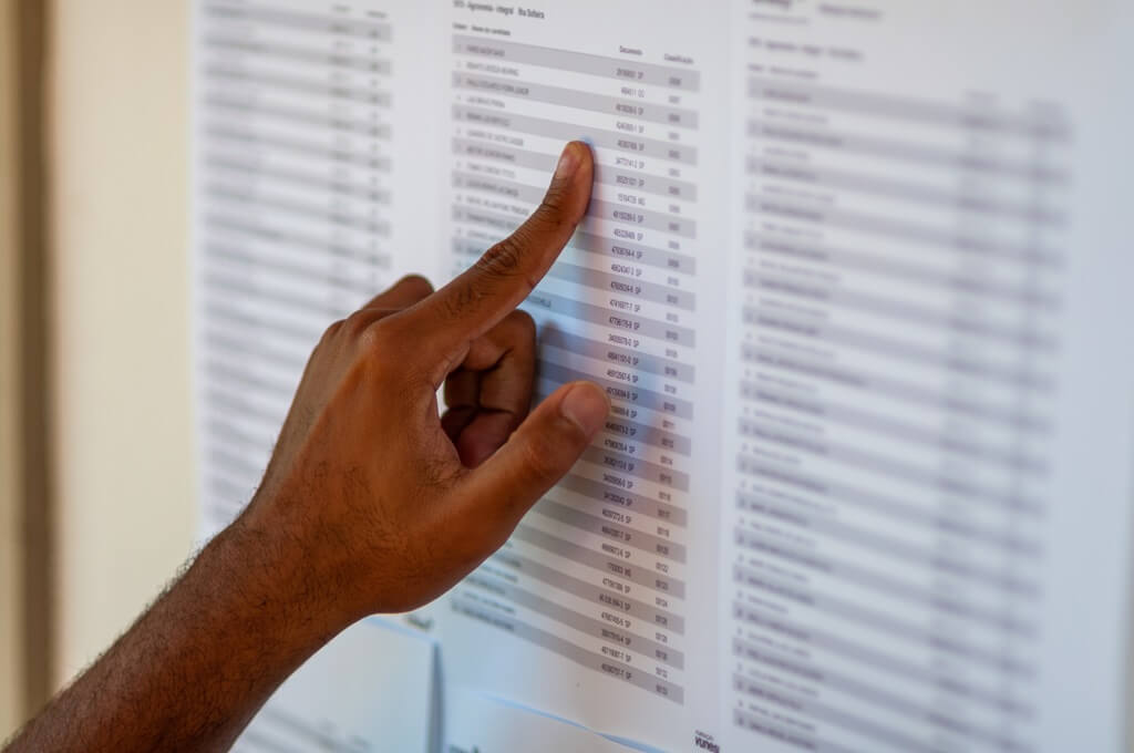 mão de rapaz checando lista de nomes na parede