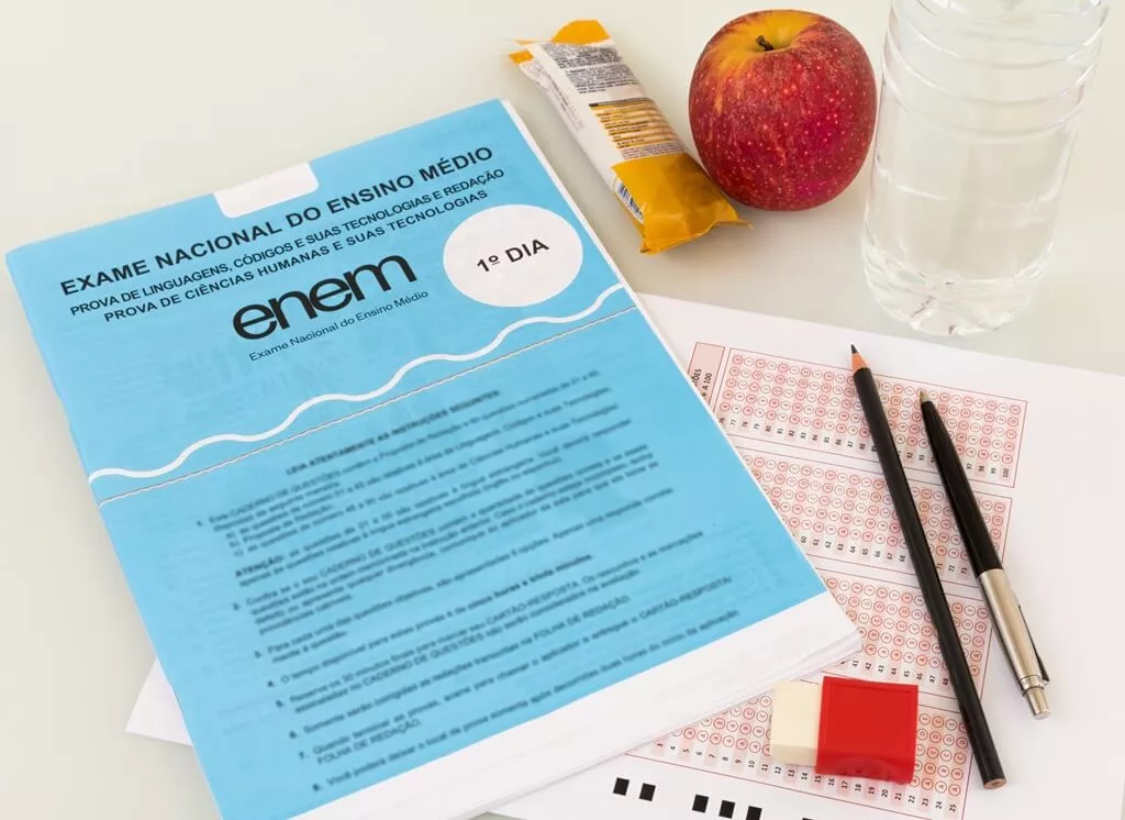 materiais de estudo em cima de prova do enem, ao lado de barrinha, maçã e garrafa de água