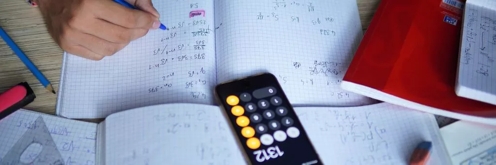 pessoa fazendo contas de matemática ao lado de livros e calculadora